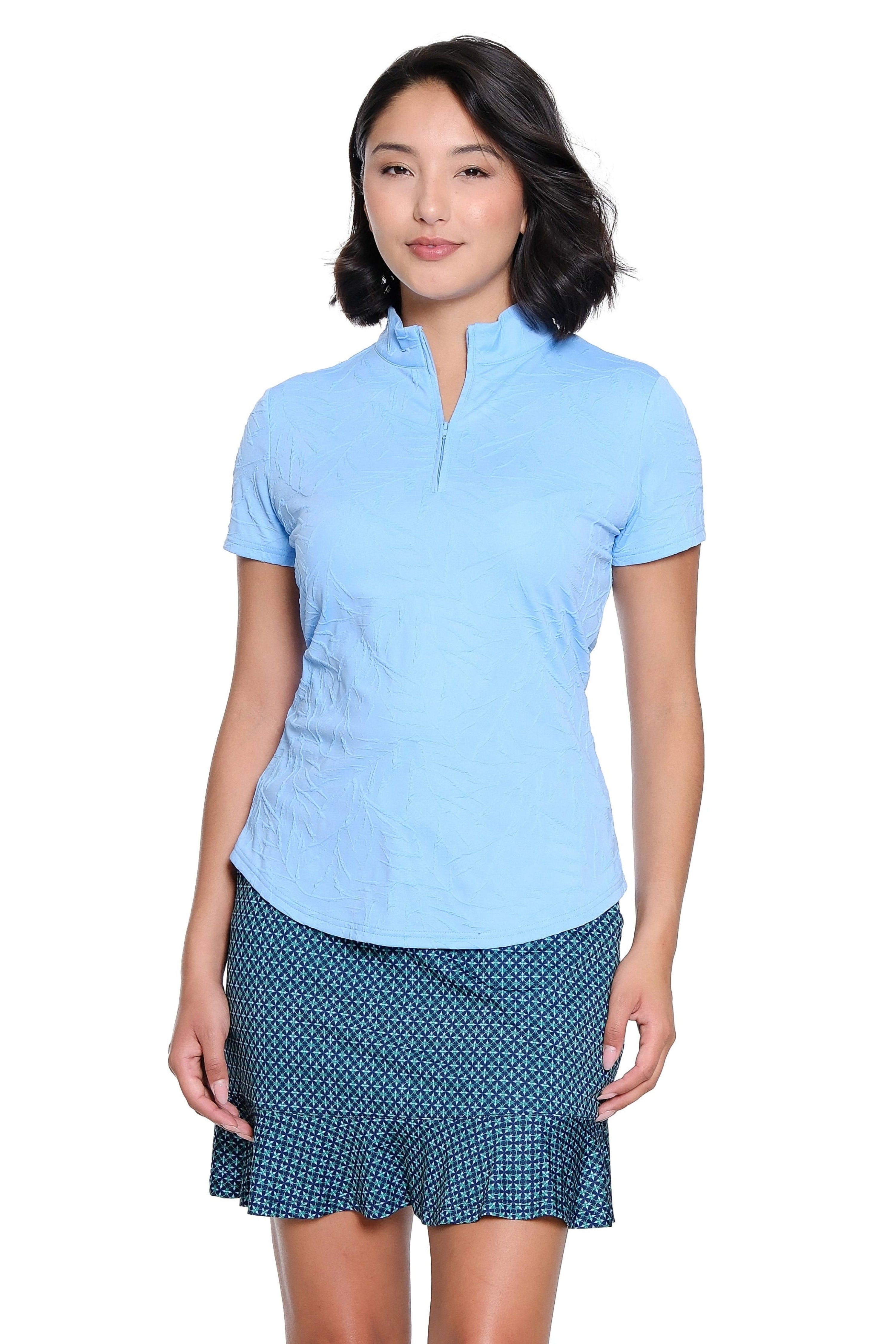 Woman wearing a light blue polo shirt and navy patterned skirt on a white background
